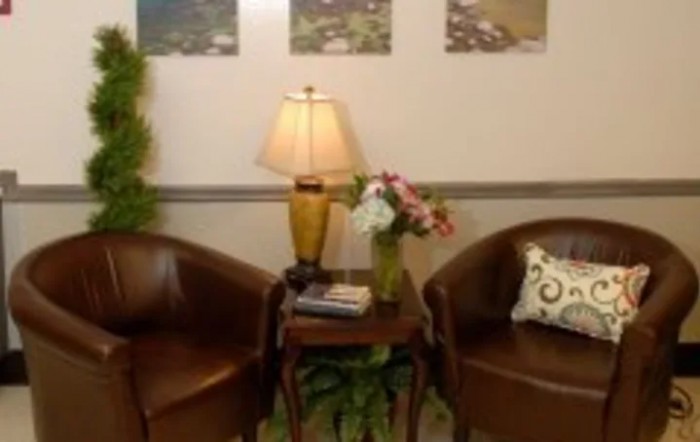 A cozy lobby area with two leather chairs, a small table with a lamp, and a vase of flowers.