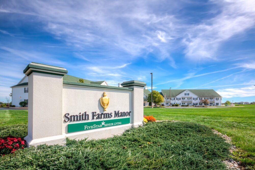 Entrance sign for Smith Farms Manor with a building in the background under a blue sky.