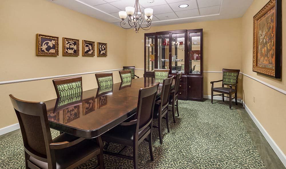 A formal dining room with a long table, surrounded by chairs and a cabinet in the background.