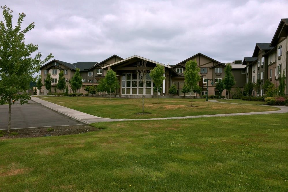 A large building with a modern architectural design surrounded by a grassy lawn and trees under a cloudy sky.