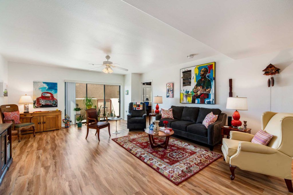 A spacious living room with stylish decor, featuring a sofa set, vibrant artwork, and a patterned rug on a wooden floor.
