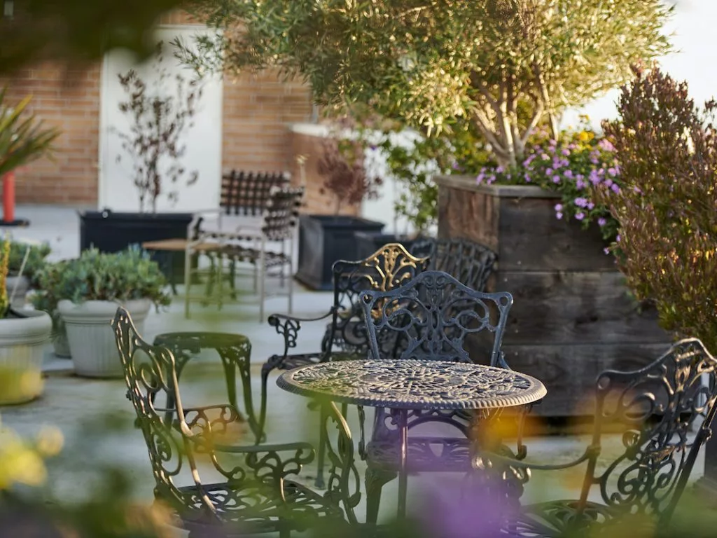A tranquil garden setting with ornate iron furniture surrounded by lush plants.