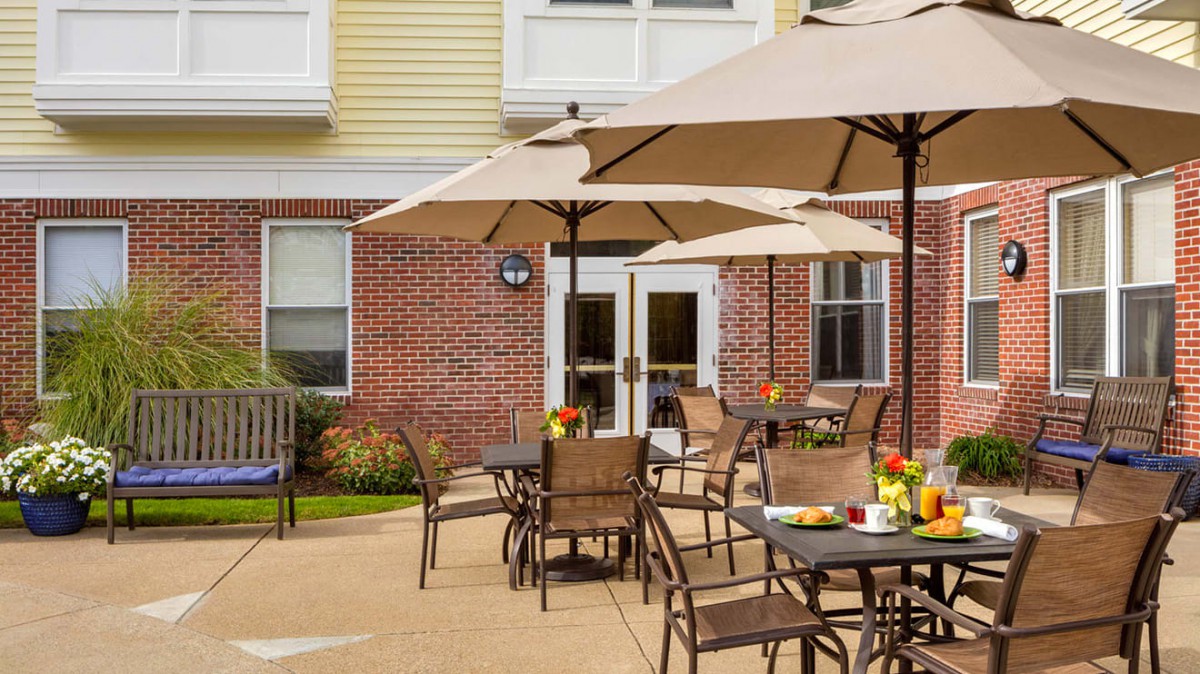 An inviting outdoor patio area with tables, chairs, and umbrellas in front of a brick building.
