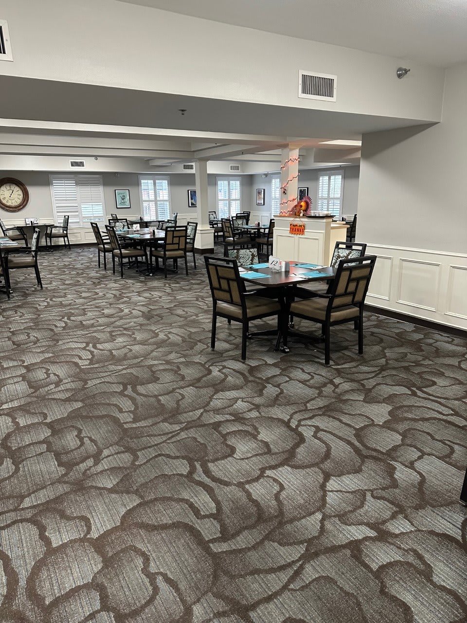 An empty dining area with multiple tables and chairs on a patterned carpet.