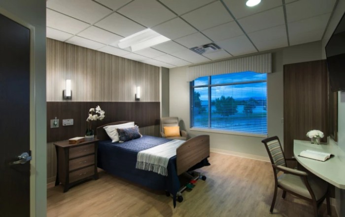 A modern hospital room with a single bed, nightstand, and large window.