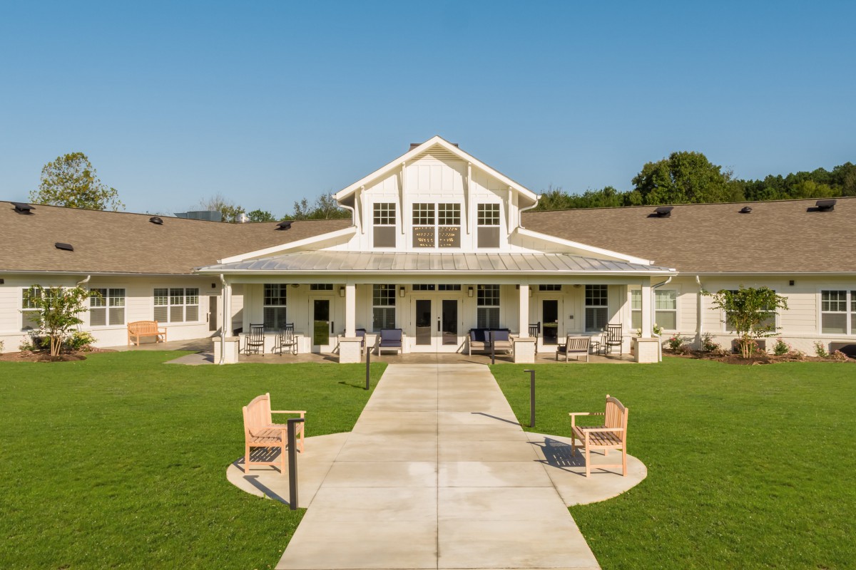 A picturesque view of a house with a spacious lawn and benches.