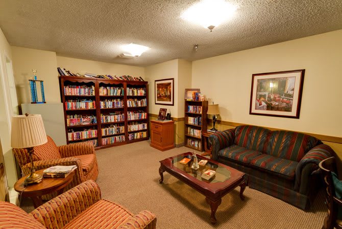 A cozy living room with bookshelves, a couch, and armchairs arranged around a coffee table.