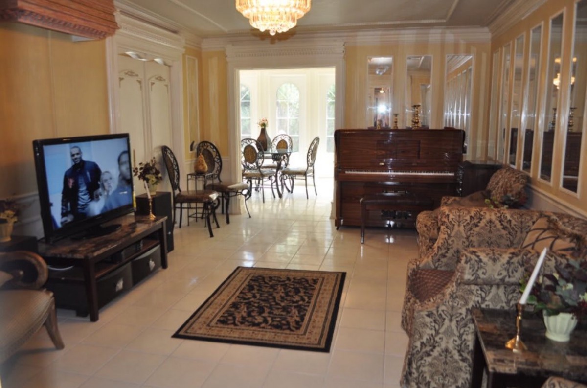 A cozy living room features a piano, television, and elegant chandelier with a view into the dining area.