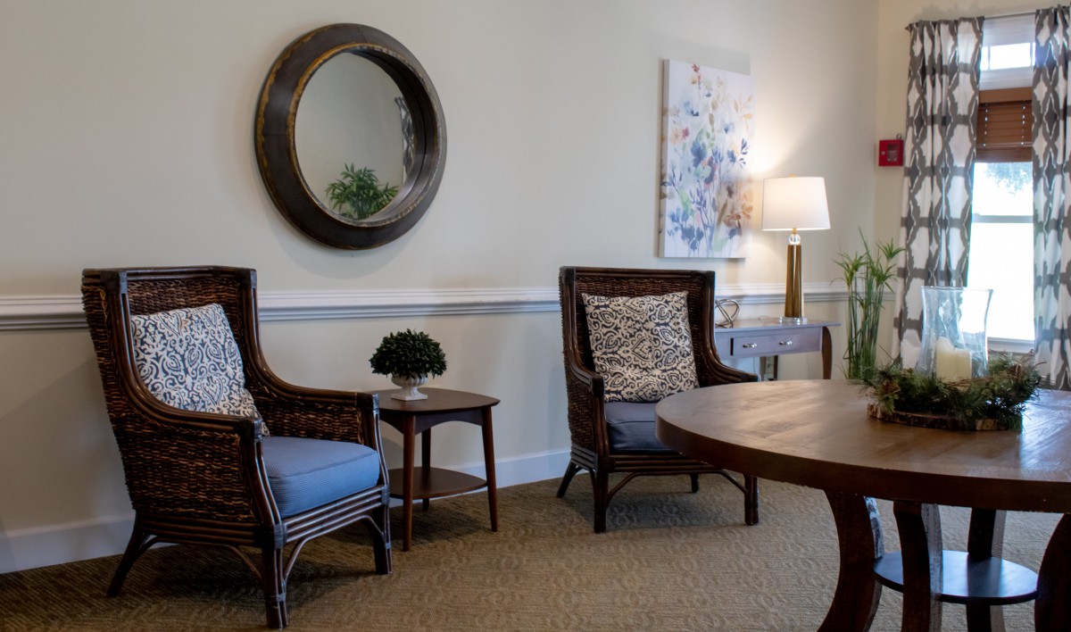 A cozy living room area with wicker chairs, a round mirror, and tasteful decor.