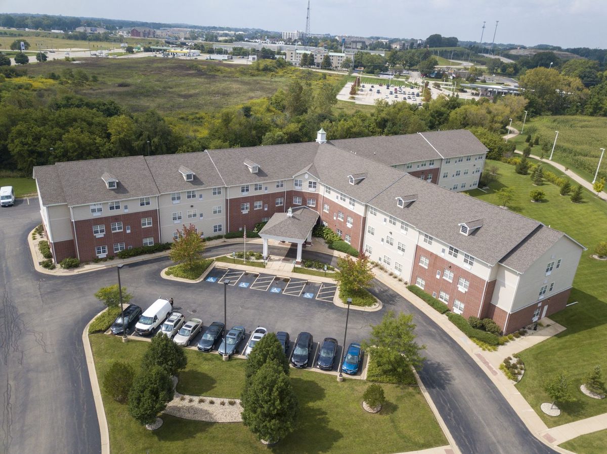 Aerial view of a residential building with a parking lot in a suburban area surrounded by greenery.