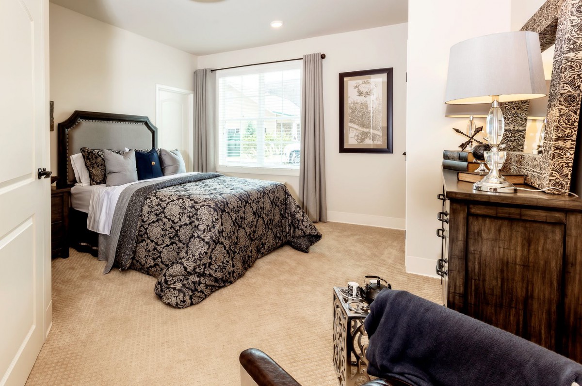 A cozy and elegantly decorated bedroom with patterned bedding, a large window, and stylish furnishings.