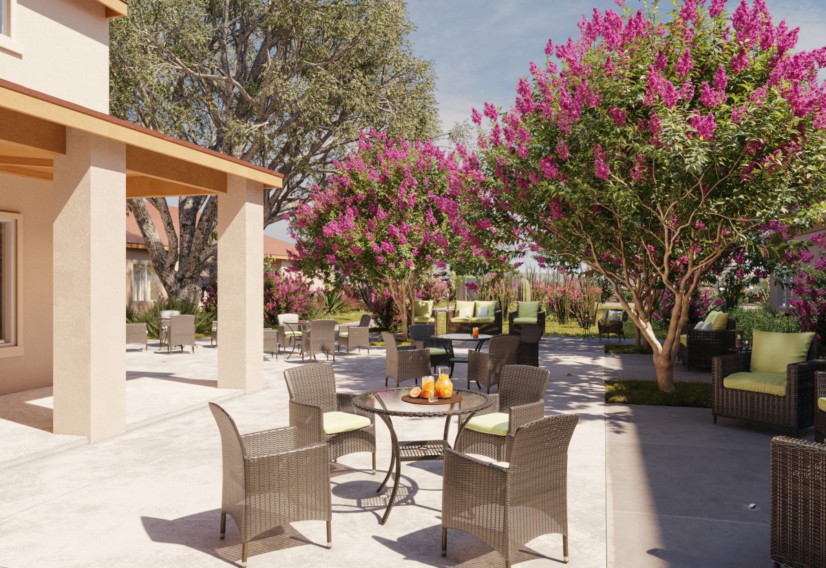 A peaceful outdoor patio area with wicker furniture surrounded by blooming trees and vibrant flowers.