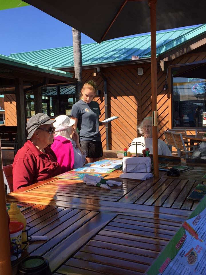 A group of people seated at an outdoor restaurant, looking at menus while a server takes their order.