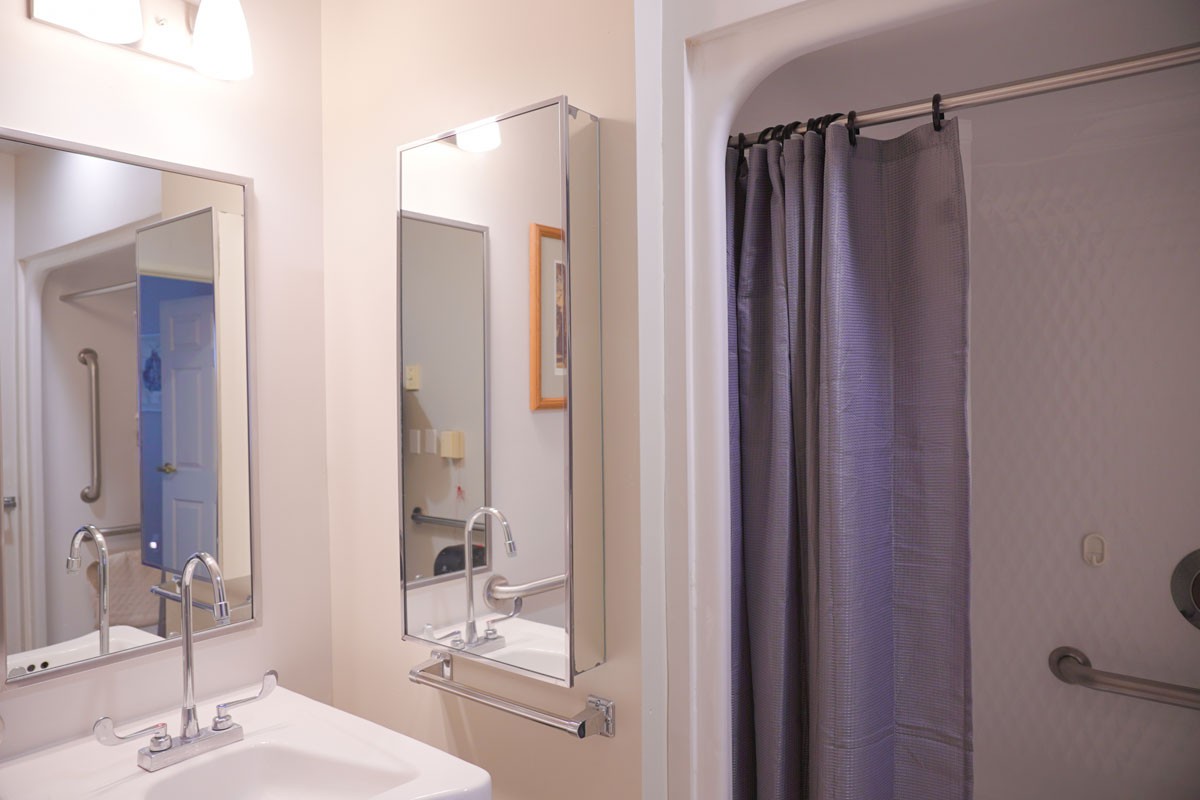 A clean and tidy bathroom featuring a mirror, sink, and shower with a gray curtain.