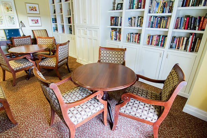 A cozy library area with a wooden table and upholstered chairs surrounded by bookshelves.