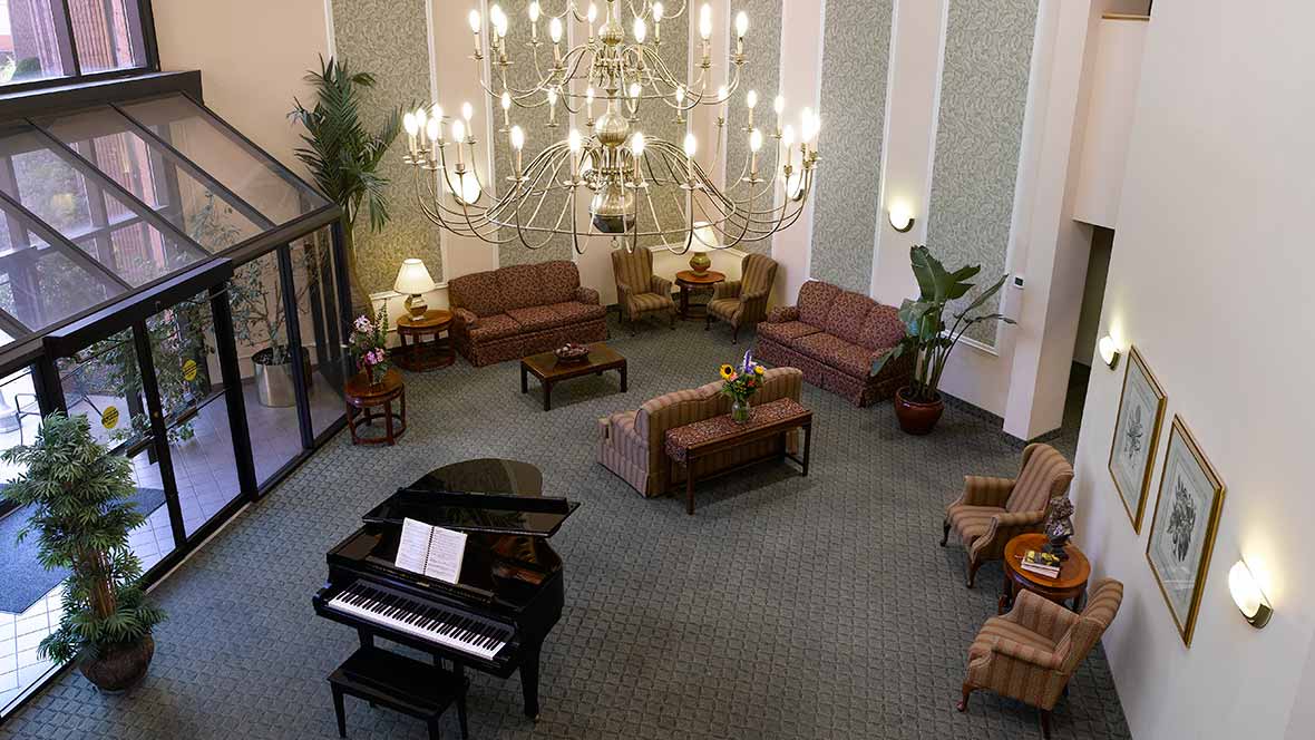 A spacious lobby featuring a grand piano, elegant chandelier, and comfortable seating area.