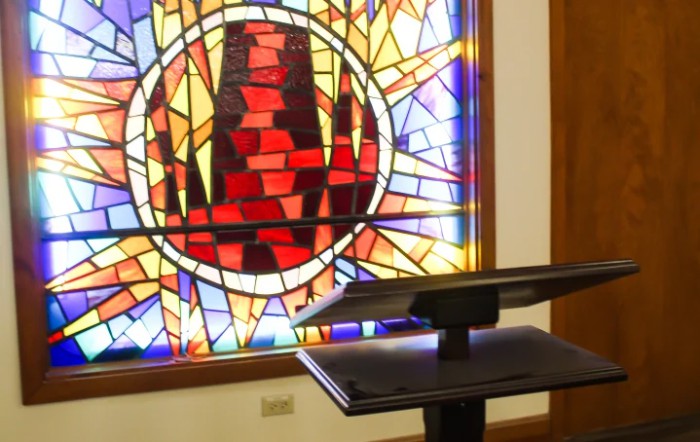 A church podium stands in front of vibrant stained glass artwork.