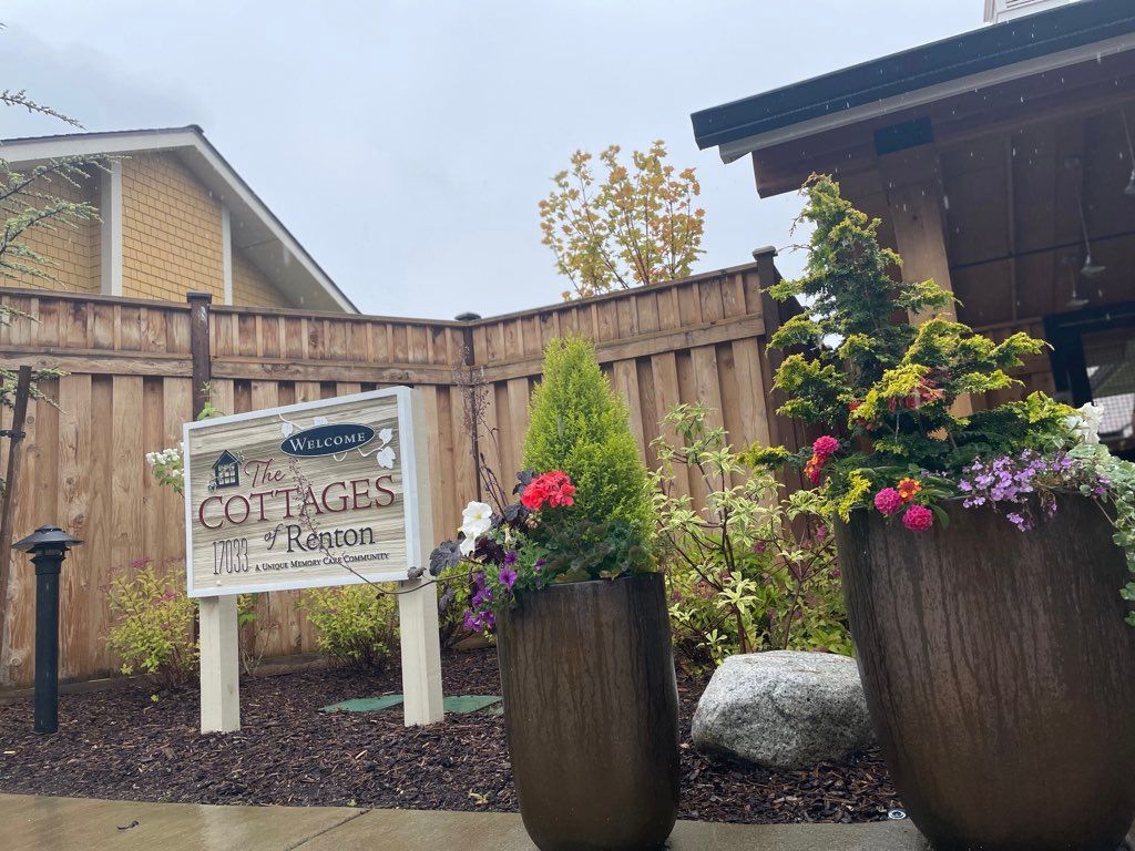 Entrance of a cottage property with planters and flowers next to a wooden fence.