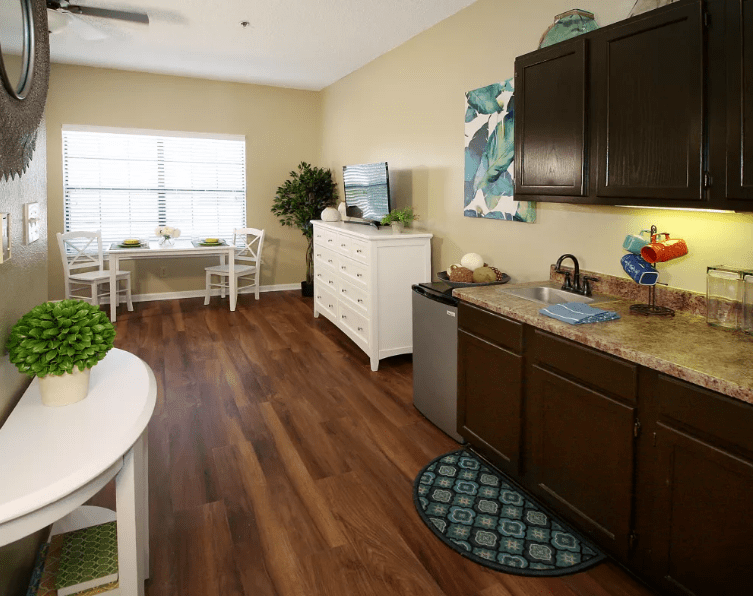 A cozy kitchen and dining area with hardwood floors, featuring dark cabinets, a small table with chairs, and a window letting in natural light.