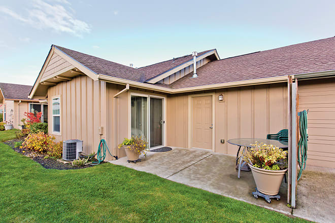 A backyard view of a house featuring a patio area with outdoor furniture and potted plants on a grassy lawn.
