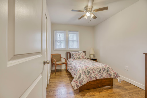 A cozy bedroom featuring a bed with floral bedding, a wooden chair, and a ceiling fan.