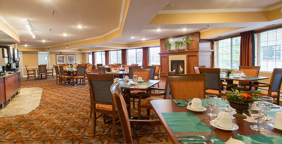 A spacious dining area with neatly arranged tables and chairs, featuring a warm fireplace and large windows.