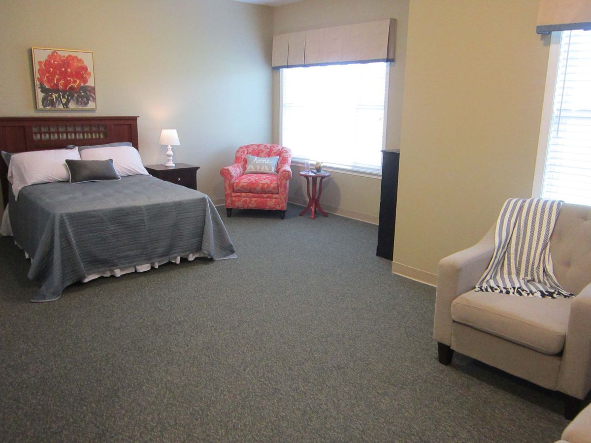 A cozy bedroom with a bed, two chairs, and a large window allowing natural light.