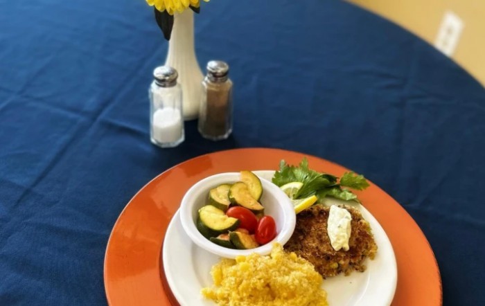A breakfast plate featuring scrambled eggs, hash browns, and a side of zucchini and tomato salad is elegantly set on a table with salt, pepper, and a small vase with yellow flowers.