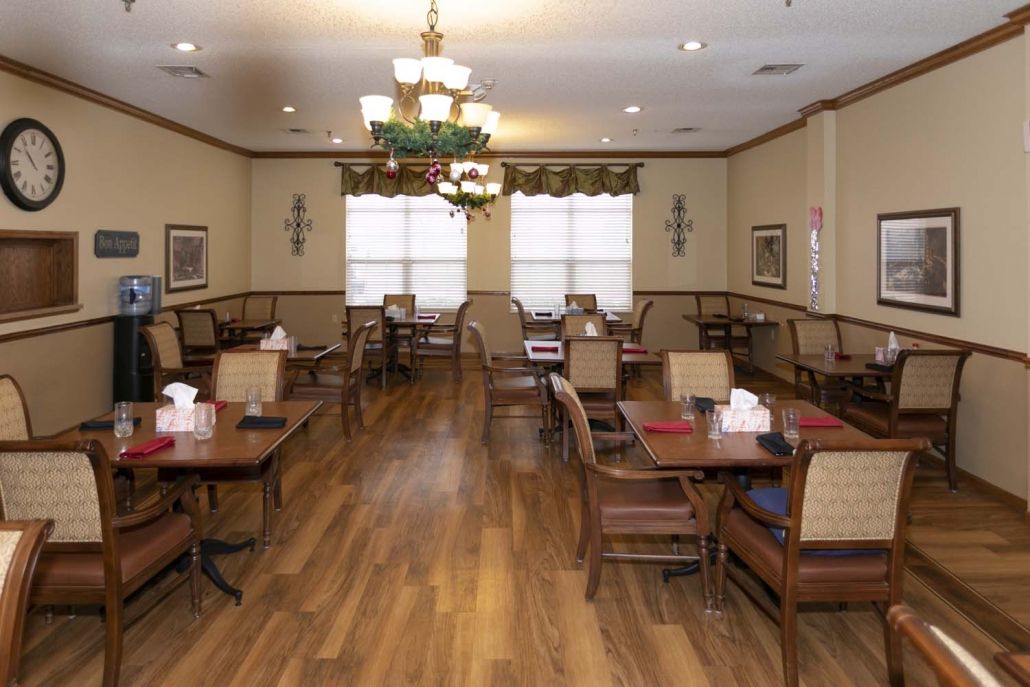 A cozy dining room with wooden floors, multiple tables and chairs, and elegant chandeliers.