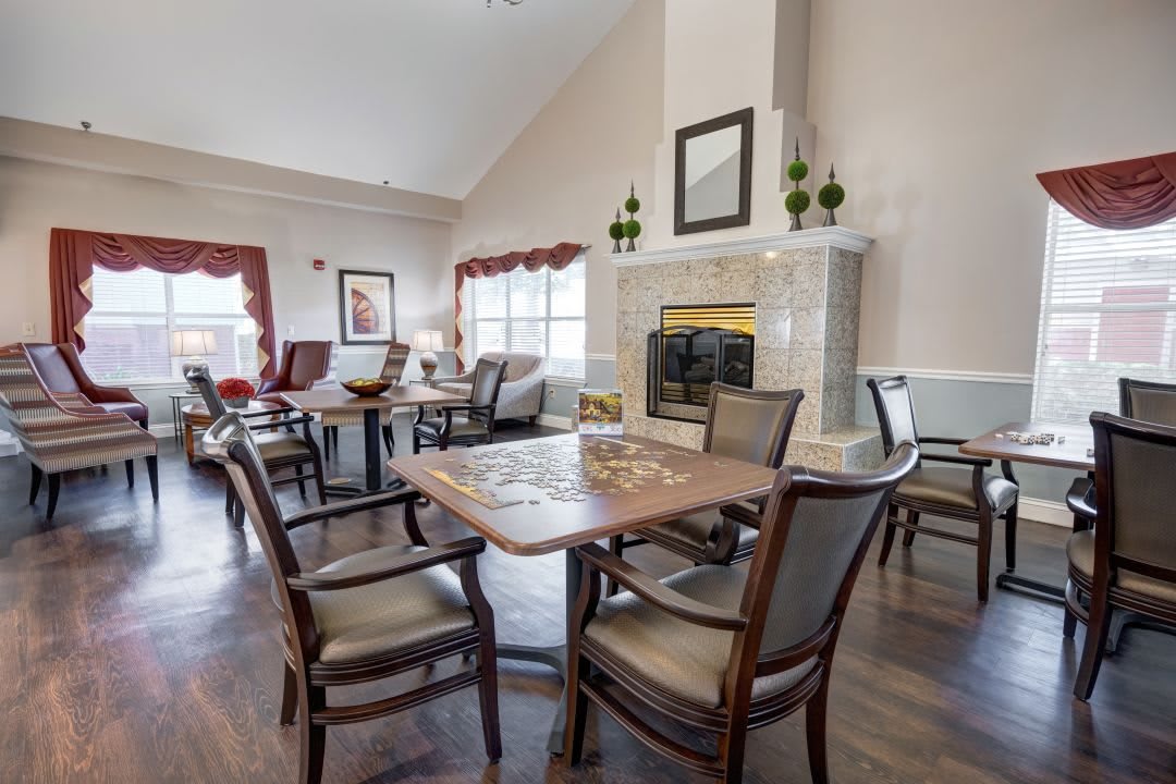 A cozy living room with tables and chairs arranged around a fireplace.