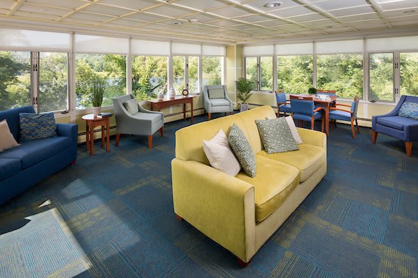 A bright lounge area featuring a yellow sofa, various chairs, and large windows letting in natural light.