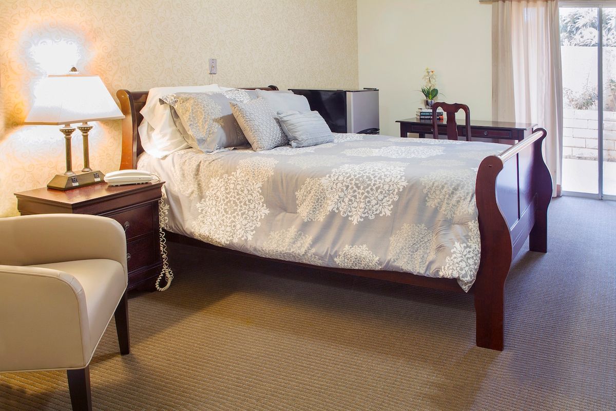 A cozy bedroom with a neatly made bed, nightstand, and comfortable chair.