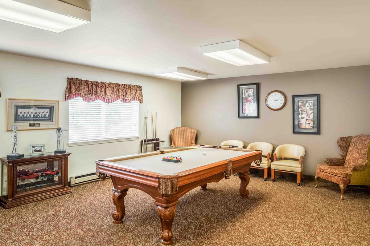 A cozy game room featuring a pool table, comfortable chairs, and framed wall art.