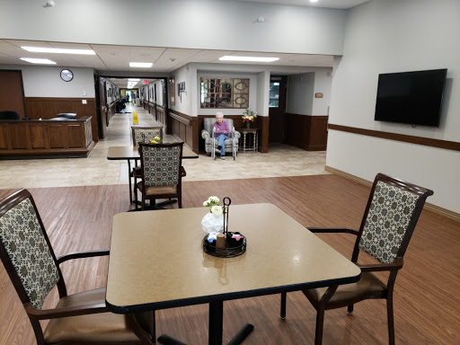 A cozy common area in a healthcare facility featuring tables, chairs, and a long corridor.