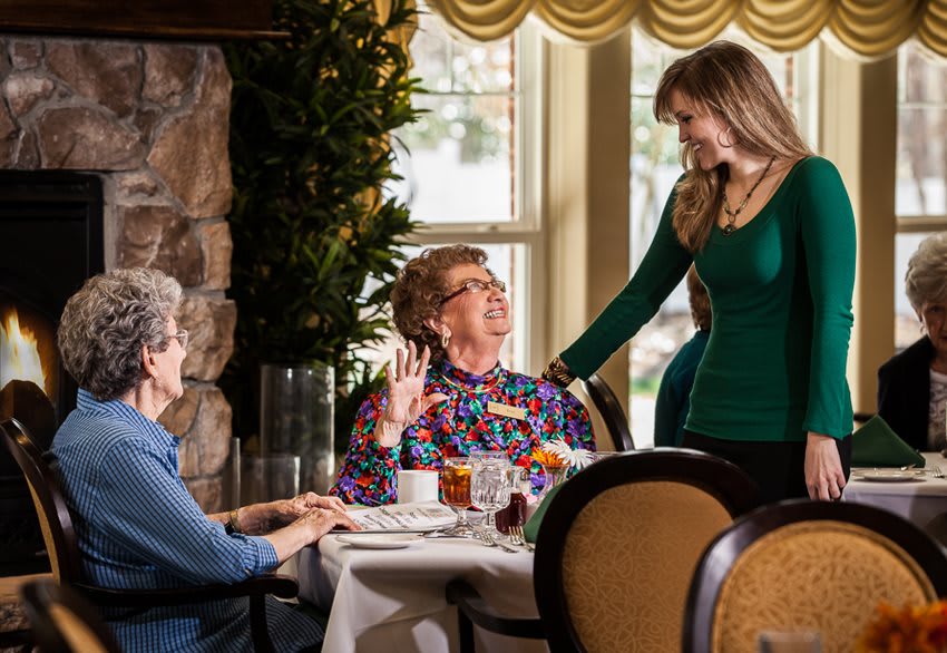 Three women engaged in conversation at a dining table indoors.