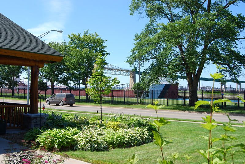 A scenic view of a bridge in the background with trees, a road, and well-maintained lawns in the foreground.