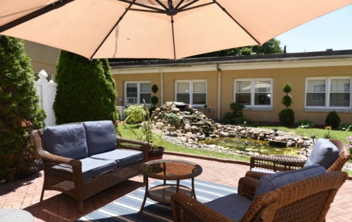A cozy patio area with wooden furniture and a large umbrella, overlooking a landscaped garden.