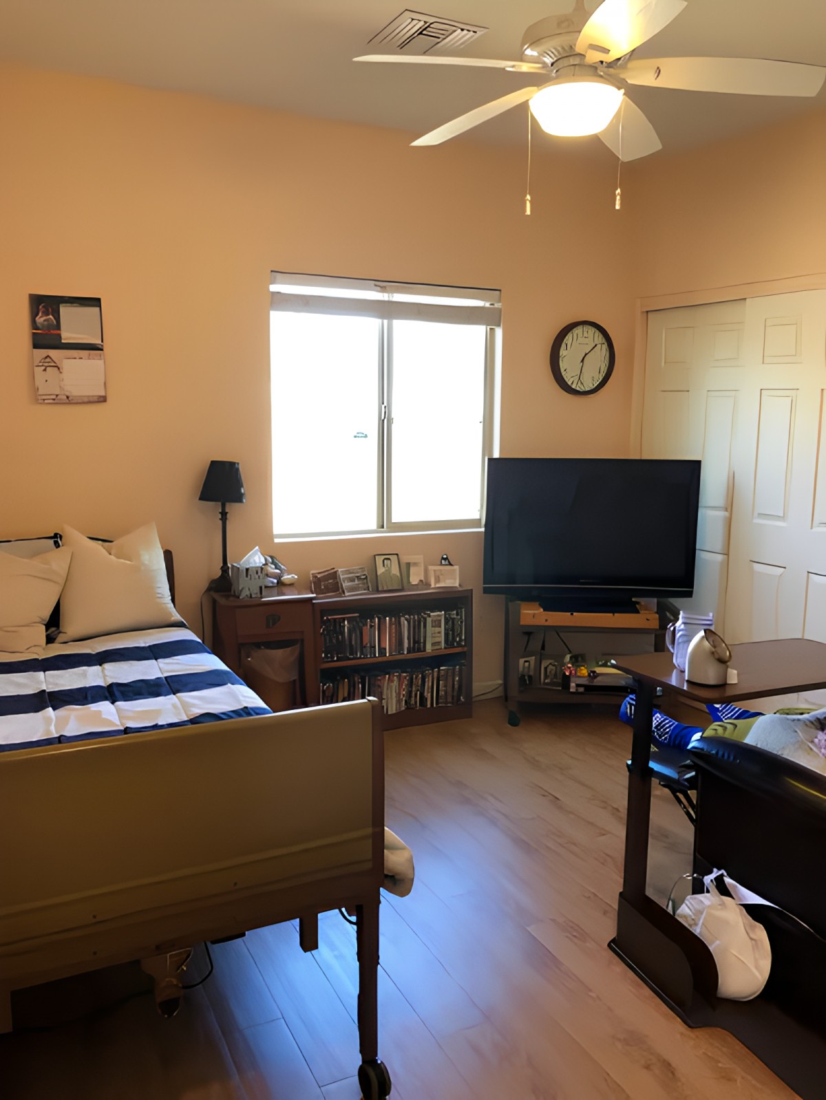 A cozy bedroom with a bed, television, and bookshelf by the window.