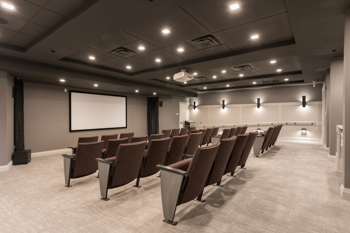 An empty auditorium with rows of seats facing a large screen.