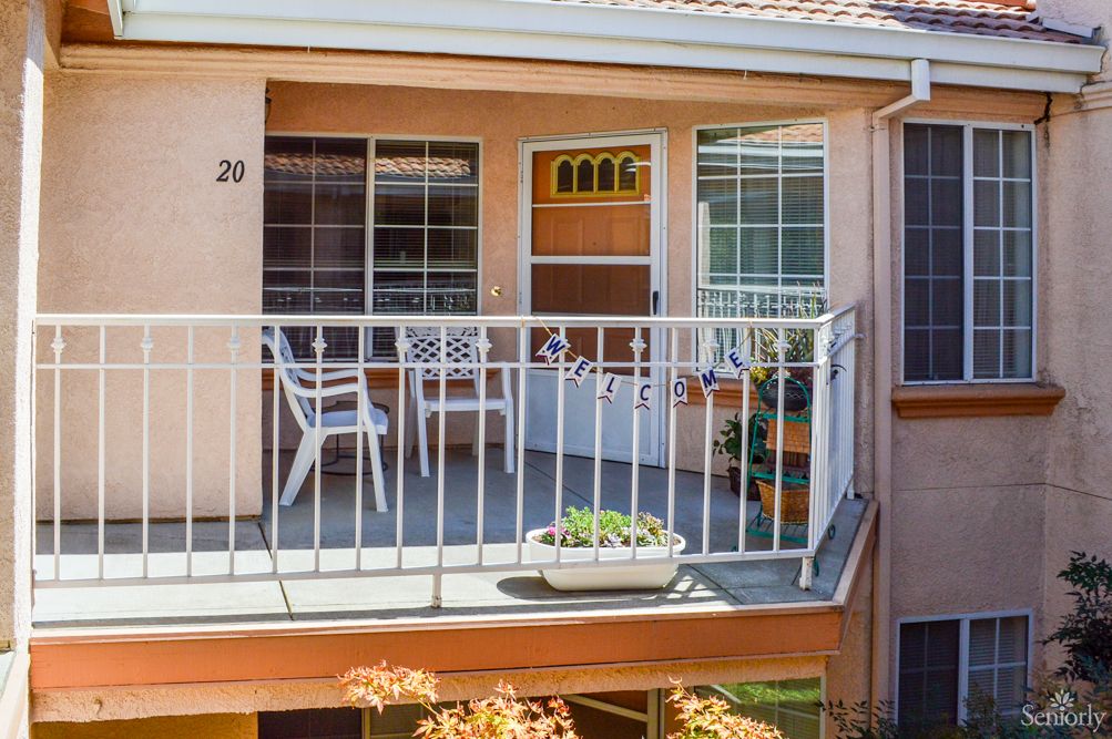 A cozy apartment balcony featuring chairs, a table, and potted plants.
