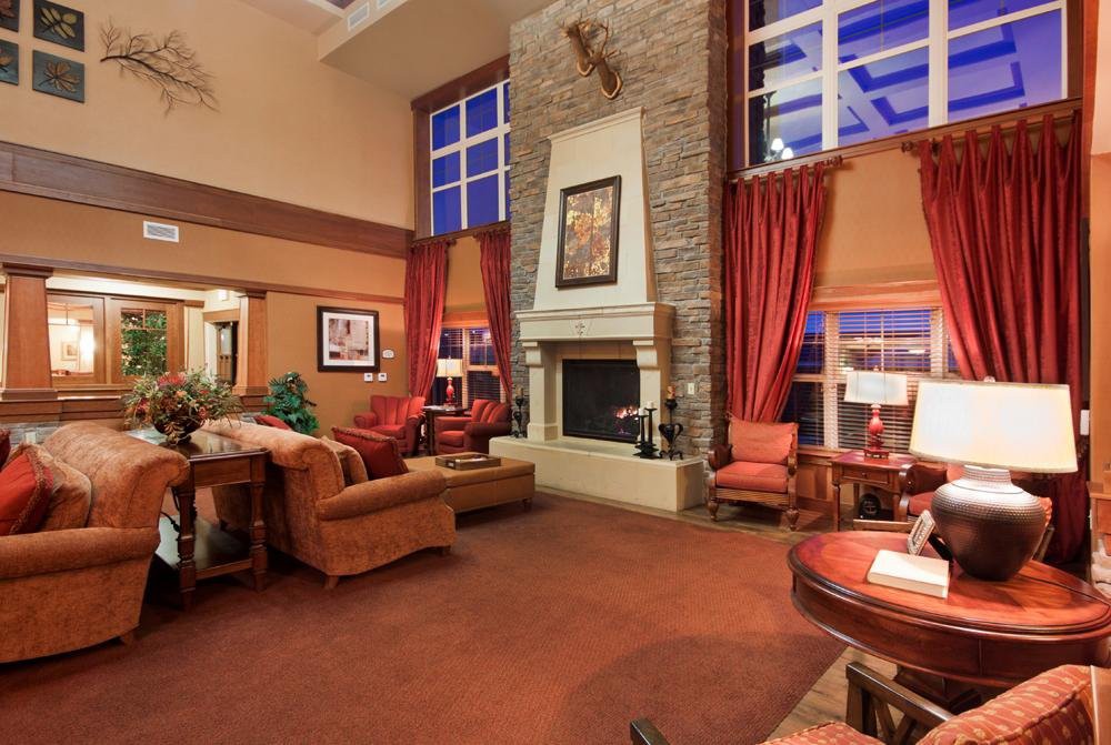 A cozy living room with a fireplace, furnished with comfortable chairs and accented by large windows and rich curtains.