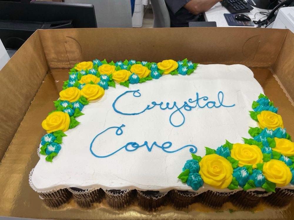 A decorated cake with 'Crystal Cove' written on it, featuring yellow roses and blue flowers.