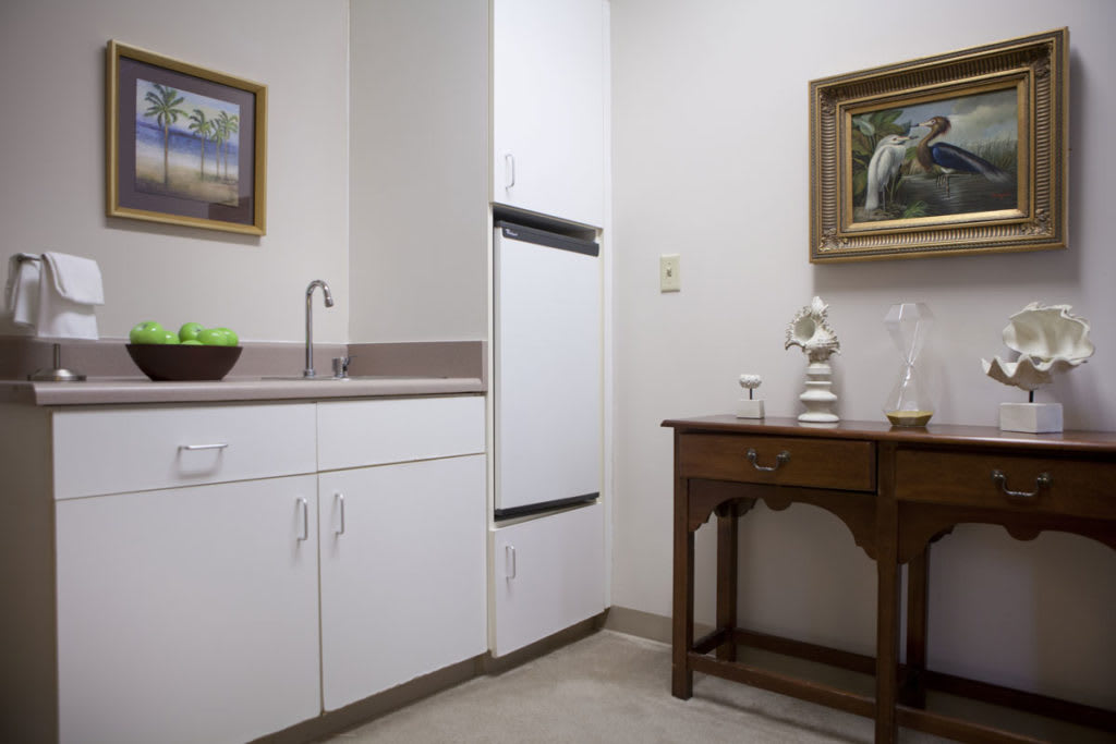 A small kitchenette area with white cabinets, a sink, and decorative artwork on the walls.