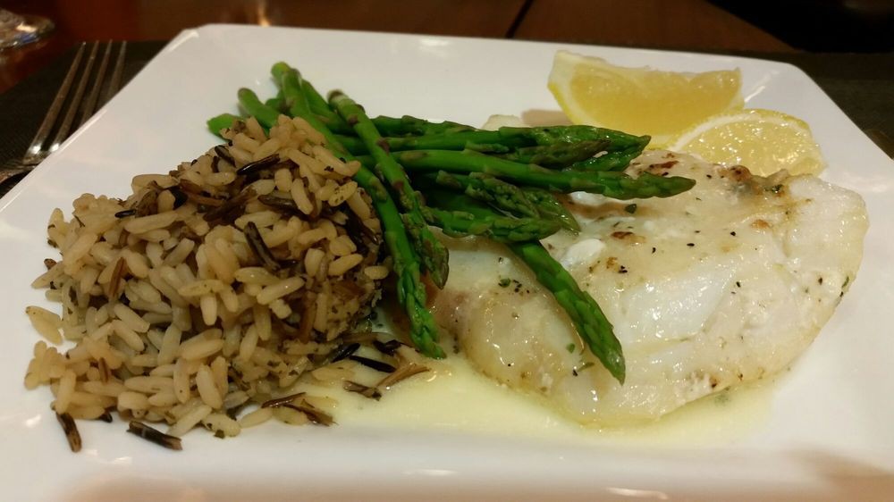 A plate featuring fish with a side of asparagus, wild rice, and a lemon wedge.