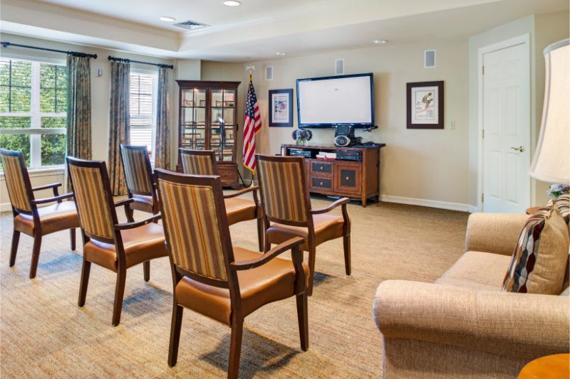 A small conference room with arranged chairs facing a television, featuring a flag and cabinet.