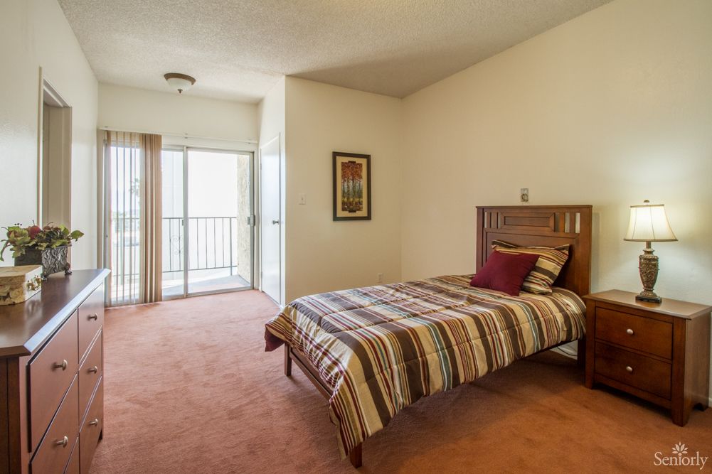 A minimalist bedroom featuring a single bed with striped bedding, a decorative pillow, and natural light coming through an open sliding door.
