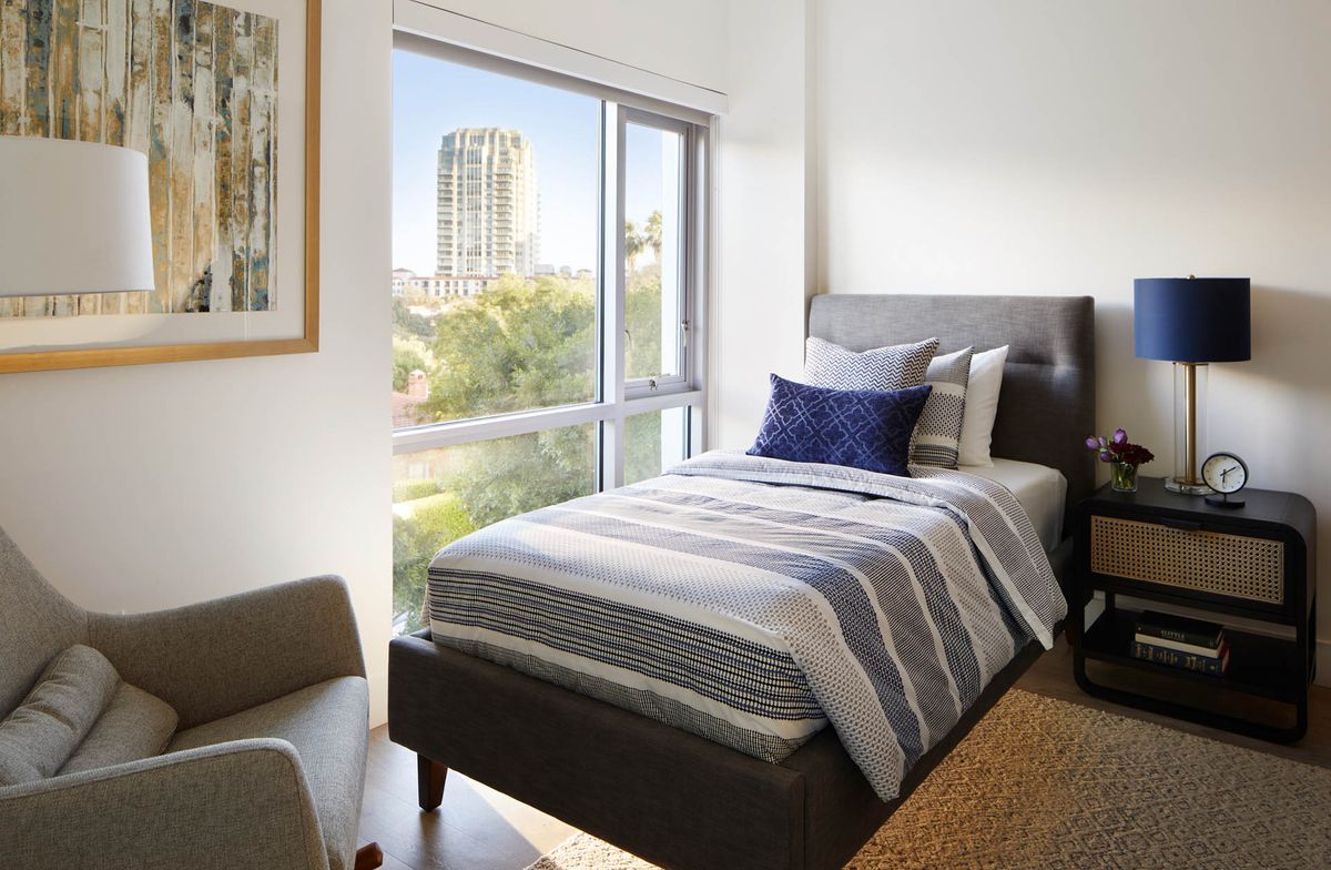 A modern bedroom with a single bed and large window offering a city view.