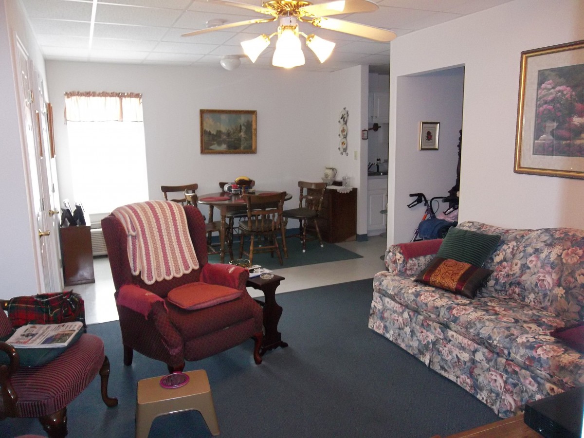 A cozy living room with a floral sofa and armchair, adjacent to a dining area featuring a wooden table and chairs.
