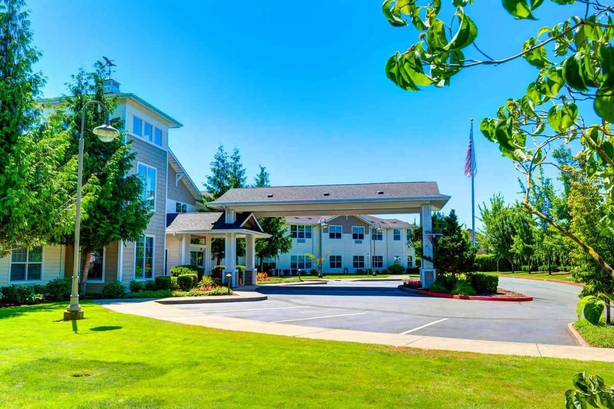 A sunny view of a hotel entrance surrounded by trees and a well-maintained lawn.