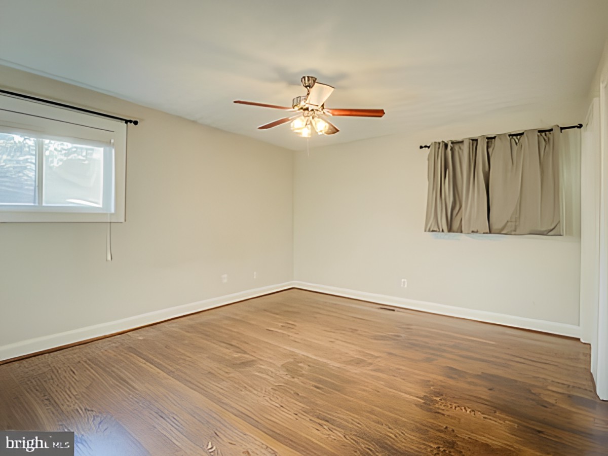 An empty room with hardwood floors and a ceiling fan.